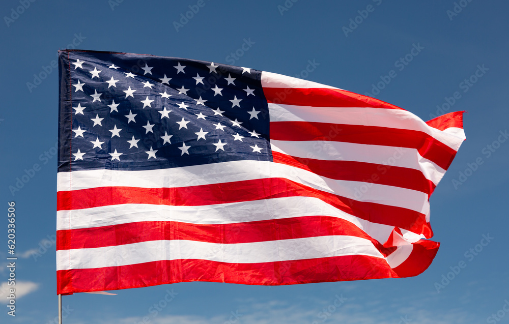 Fototapeta premium Large USA flag flying against clear blue sky and clouds