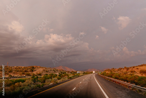 A beautiful asphalt road among hills with dry grass. A scenic landscape with highway, mountains on background and blue sky with fluffy clouds on sunny day. Phoenix, AZ, USA - 7-22-2021