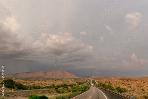 A beautiful asphalt road among hills with dry grass. A scenic landscape with highway, mountains on background and blue sky with fluffy clouds on sunny day. Phoenix, AZ, USA - 7-22-2021