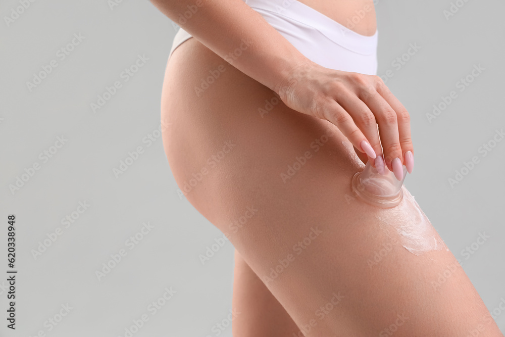 Young woman applying anti-cellulite cream on her leg against light background, closeup