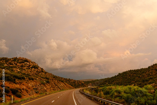 A beautiful asphalt road among hills with dry grass. A scenic landscape with highway, mountains on background and blue sky with fluffy clouds on sunny day. Phoenix, AZ, USA - 7-22-2021