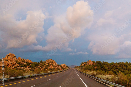 A beautiful asphalt road among hills with dry grass. A scenic landscape with highway, mountains on background and sunset sky. Phoenix, AZ, USA - 7-22-2021