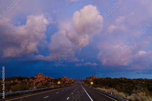 A beautiful asphalt road among hills with dry grass. A scenic landscape with highway, mountains on background and sunset sky. Phoenix, AZ, USA - 7-22-2021