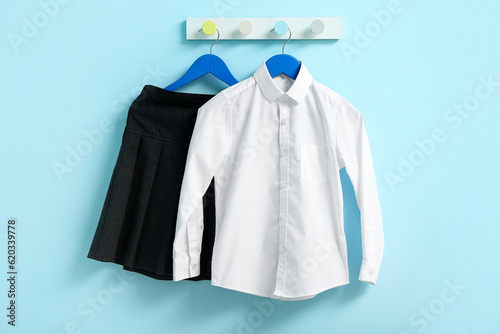 Stylish school uniform hanging on rack against blue wall