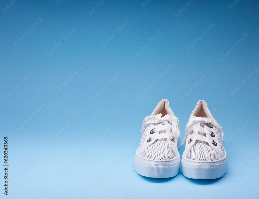 Trendy perforated leather white sneakers with thick rubber sole on the gradient blue background. Copy space. Creative minimalistic layout with footwear.