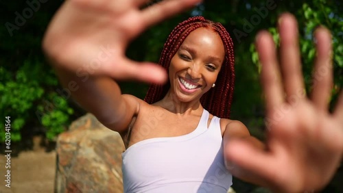 Outdoor portrait natural Beautiful young African American woman red braids hair style, perfect white teeth smile, laughing closing camera with hands at sunny summer day with green foliage background