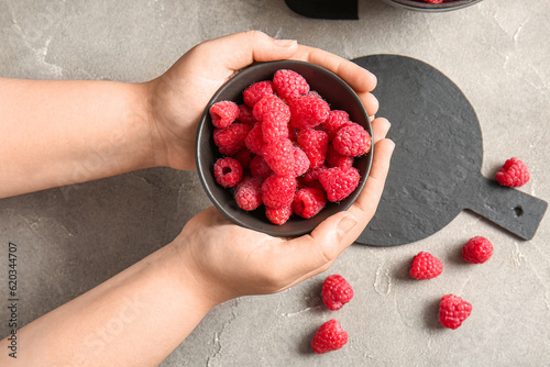 Female hands holding fresh raspberries on grey background