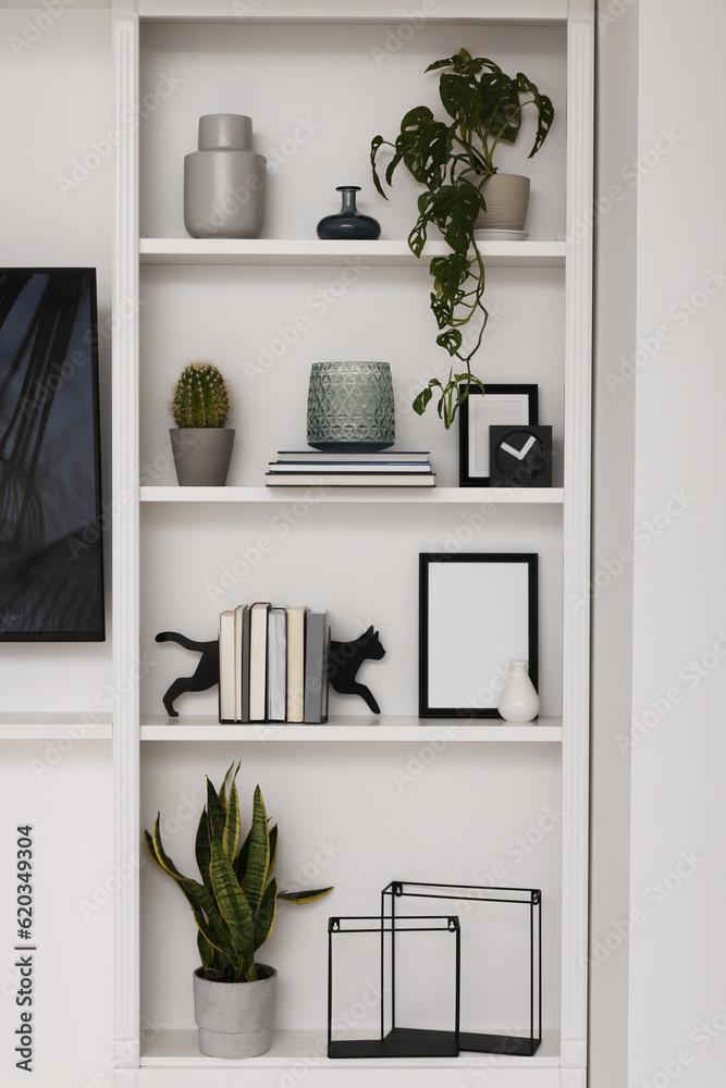 Interior design. Shelves with stylish accessories, potted plants and frame near white wall Interior design. Shelves with stylish accessories, potted plants and frame near white wall