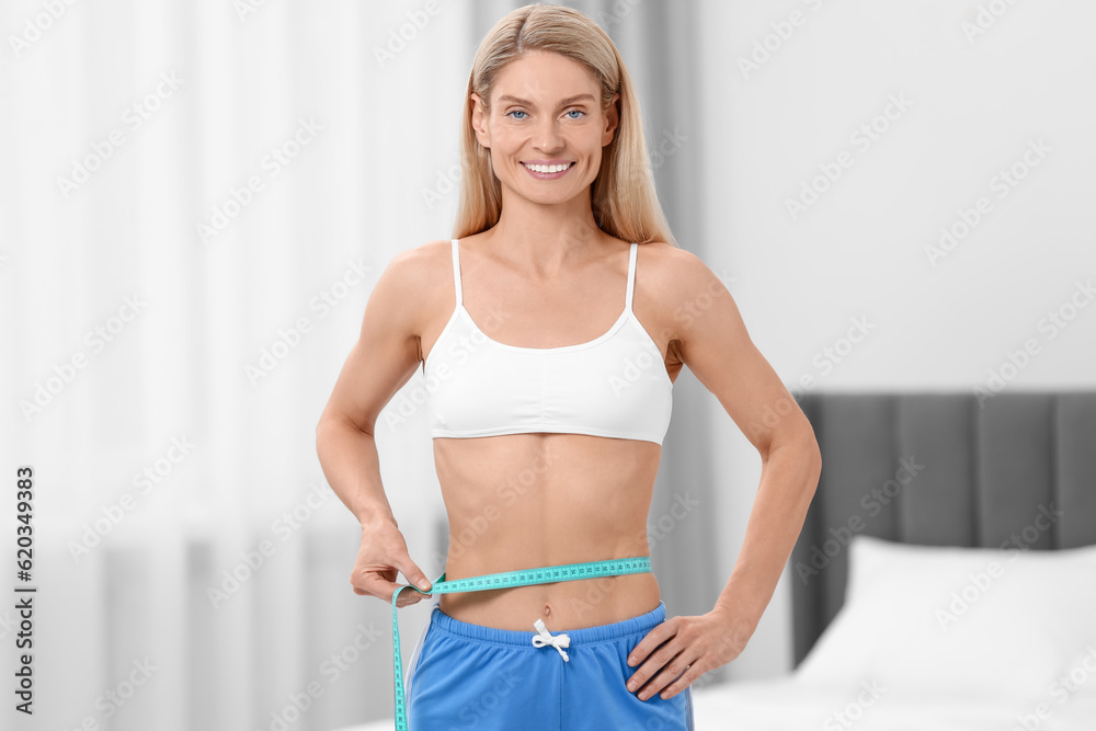 Slim woman measuring waist with tape at home. Weight loss