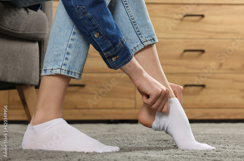 Woman putting on white socks at home, closeup