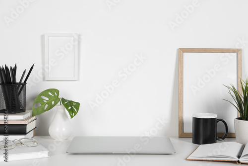 Cozy workspace with laptop, houseplants and stationery on white desk at home