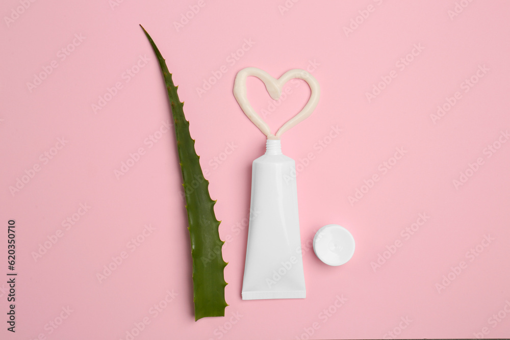 Tube of toothpaste and fresh aloe on pink background, flat lay