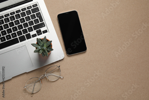 Modern laptop, houseplant, glasses and smartphone on beige table, flat lay. Space for text
