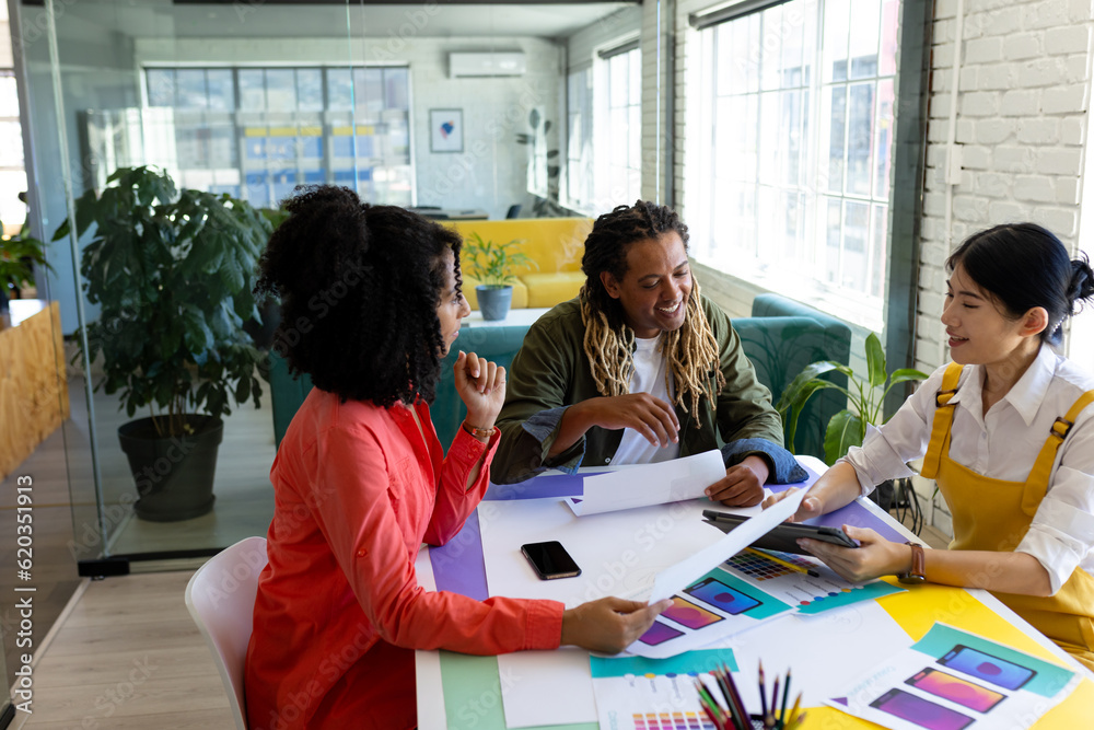 Happy diverse male and female creatives sitting at table discussing project in design meeting Happy diverse male and female creatives sitting at table discussing project in design meeting