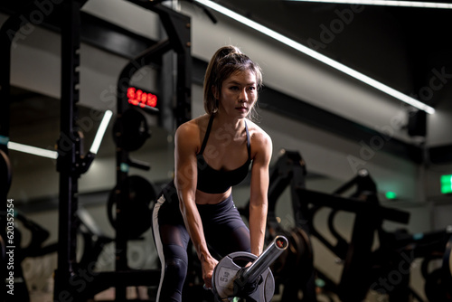 Portrait of a young Asian woman, good-looking, shapely, in a black dress. She's working exercise fitness out in a world-class gym, work hard.