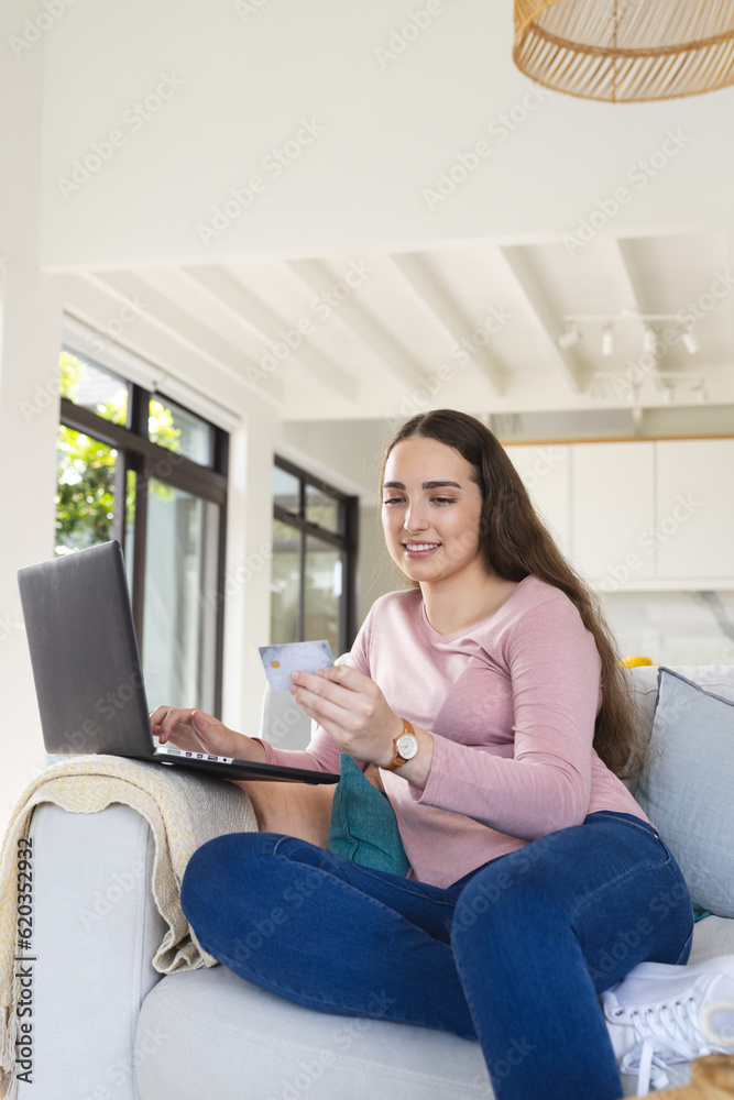 Happy caucasian woman on couch using laptop and holding credit card at home Happy caucasian woman on couch using laptop and holding credit card at home
