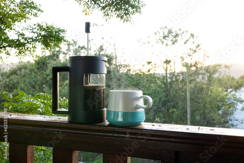 Close up of coffee press and mug of fresh coffee at balcony on sunny day