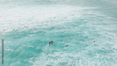 Lifeguards riding jet ski to pick up surfers in stormy ocean waters. Cinematic aerial view of men in wetsuits during surfing and shore crew working on delivering surfboards to waves forming point 4K photo