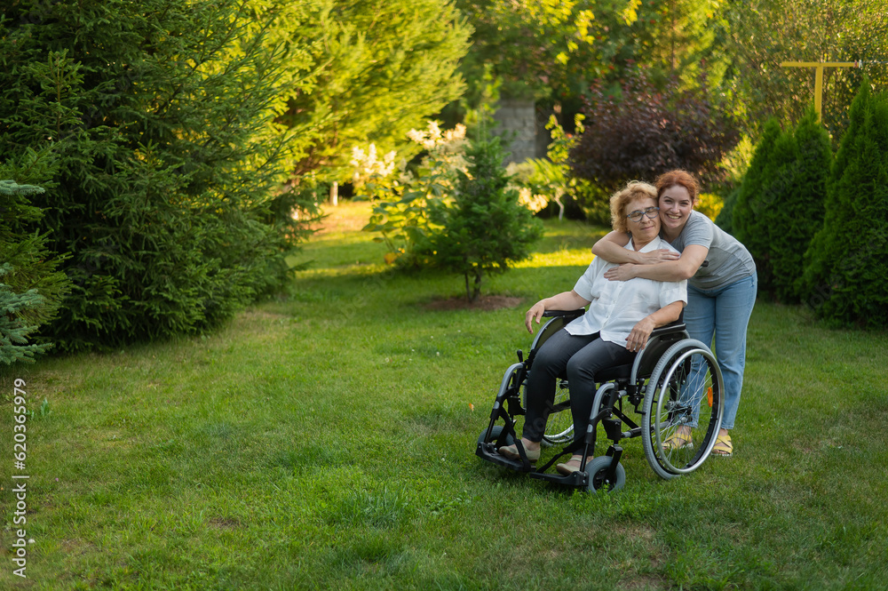 Caucasian woman hugging an elderly mother sitting in a wheelchair. Walk outdoors. Caucasian woman hugging an elderly mother sitting in a wheelchair. Walk outdoors.