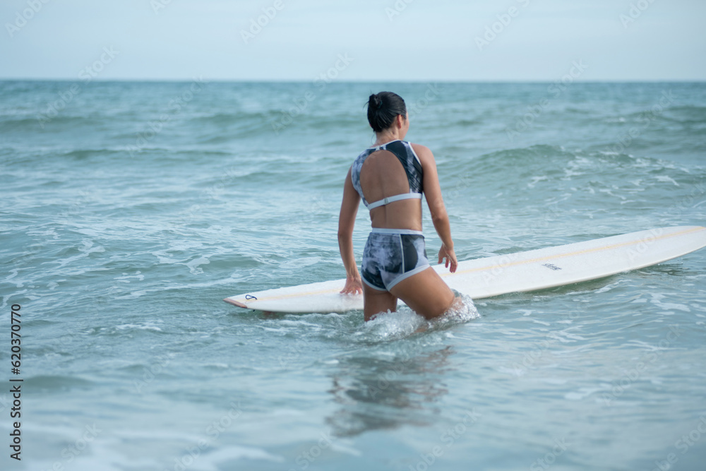 Female surfer with a surfboard entering water for surf the wave, concept of water sports activities Female surfer with a surfboard entering water for surf the wave, concept of water sports activities