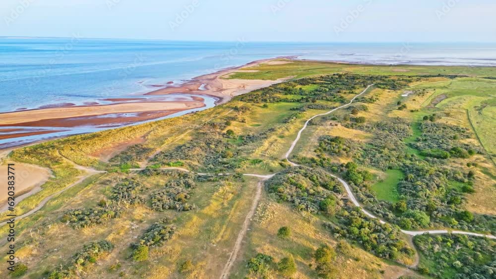 Discover the idyllic charm of a golden hour coastal scene through breathtaking aerial drone footage: estuary, sandbanks, ocean, and marshlands. Sunlit sand dunes bathe in warm sunlight. Discover the idyllic charm of a golden hour coastal scene through breathtaking aerial drone footage: estuary, sandbanks, ocean, and marshlands. Sunlit sand dunes bathe in warm sunlight.