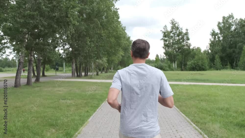 Man in gray sportwear running at park in summer. Summer health activity. Male doing active sport exercises. Man in gray sportwear running at park in summer. Summer health activity. Male doing active sport exercises.