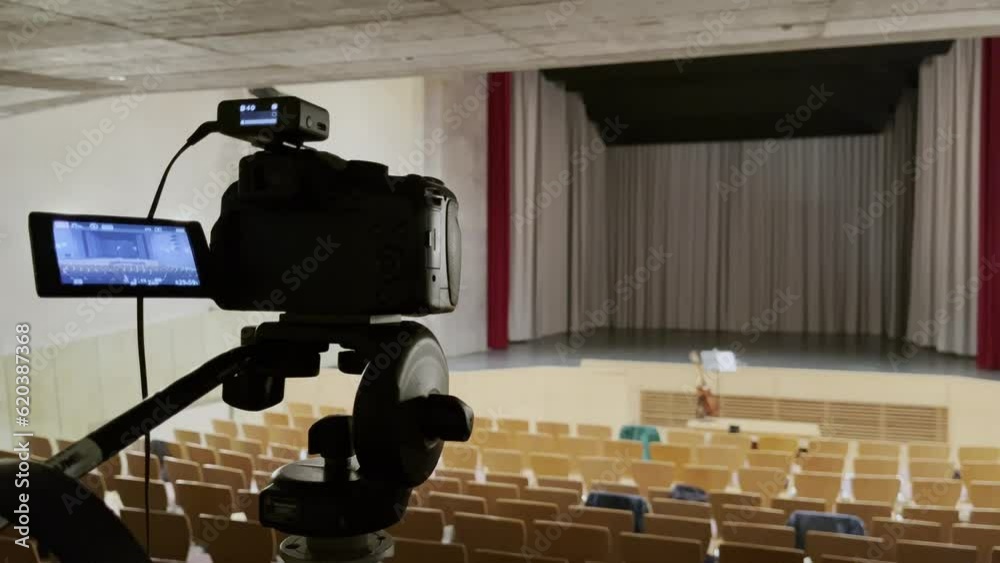 camera in an empty small concert steel with many chairs and empty stage on a tripod