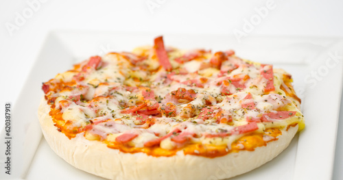 Hawaiian pizza is placed on a plate sitting on a white background.