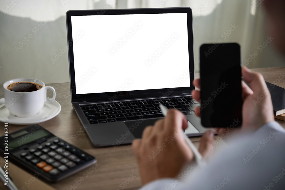 A young businessman is working on the laptop using a desktop computer with a blank screen and an empty copy space display. A young businessman is working on the laptop using a desktop computer with a blank screen and an empty copy space display.