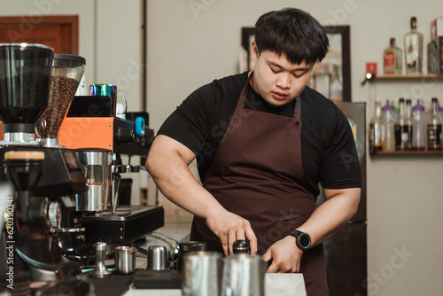 Asian man barista preparation tampering ground coffee in portafilter for espresso machine at coffee shop.. Coffee making concept.