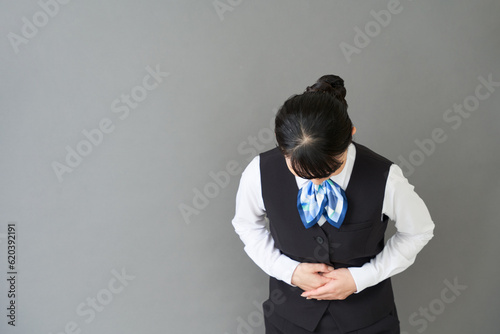 Fotografija お辞儀をするベストにリボンタイの制服を着た、受付業務、事務業務の女性