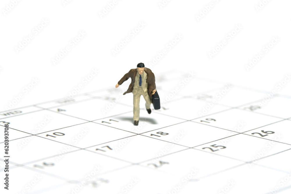 Miniature tiny people toy figure photography. A businessman running above calendar schedule carrying briefcase bag Isolated on white background Miniature tiny people toy figure photography. A businessman running above calendar schedule carrying briefcase bag Isolated on white background