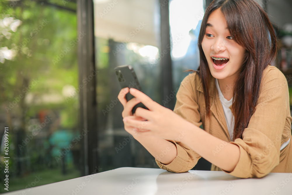 Asian woman in brown shirt looking at phone with happy expression