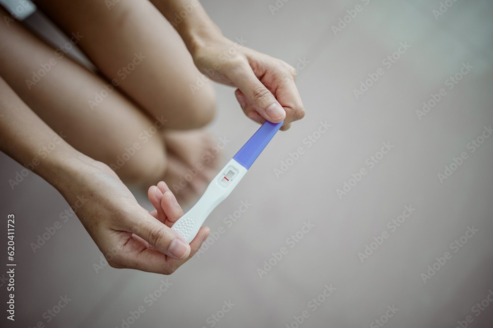 Unhappy young asian woman holding pregnancy test showing a negative result. Healthy and infertility problem concept . Unhappy young asian woman holding pregnancy test showing a negative result. Healthy and infertility problem concept .