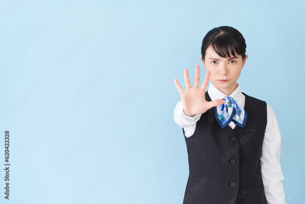 手を出して制止するベストにリボンタイの制服を着た、受付業務、事務業務の女性