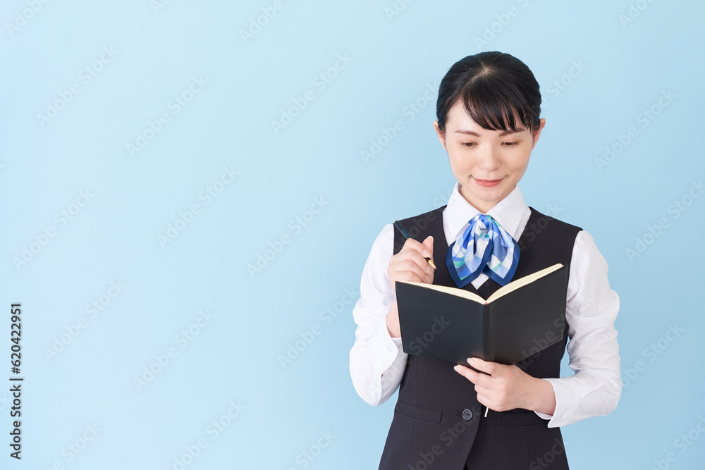 手帳を書くベストにリボンタイの制服を着た、受付業務、事務業務の女性 手帳を書くベストにリボンタイの制服を着た、受付業務、事務業務の女性