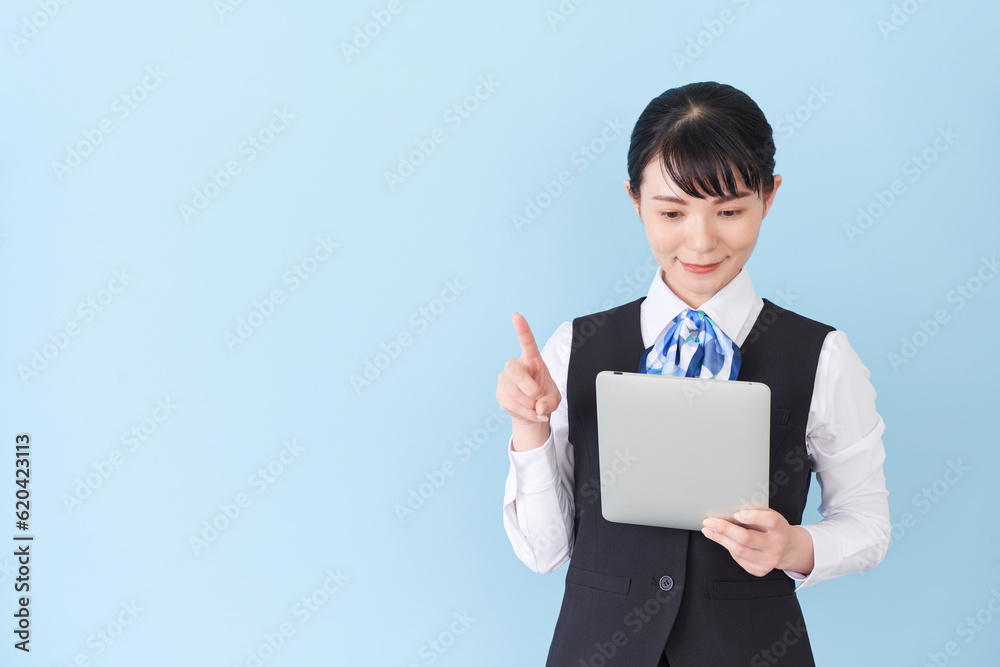 タブレットを操作するベストにリボンタイの制服を着た、受付業務、事務業務の女性 タブレットを操作するベストにリボンタイの制服を着た、受付業務、事務業務の女性