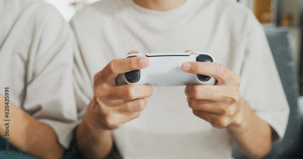 Close-up Young Asian couple sit on couch hold joystick play video game spend time together have fun at home on weekend. Happy husband and wife laugh relax with online game, Lifestyle activity concept.