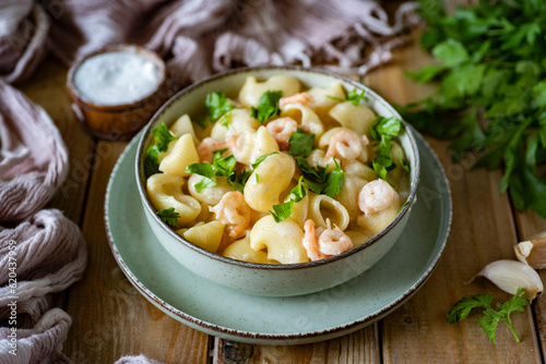 A hearty lunch or dinner for the whole family: Pasta with shrimp in a spicy cream sauce with fresh herbs in a beautiful plate on wooden boards. Close-up