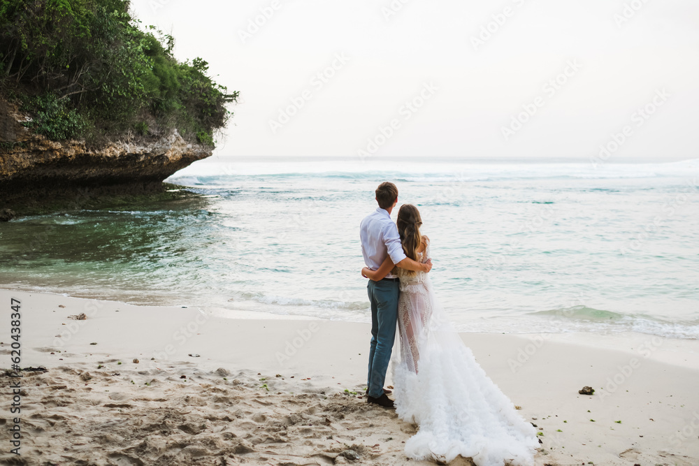 A couple of lovers, of European appearance, a man and a woman, hold hands and walk along the beach, rear view. A couple of lovers, of European appearance, a man and a woman, hold hands and walk along the beach, rear view.