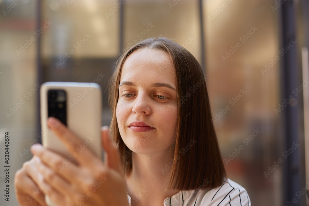 Closeup portrait of brown haired businesswoman using mobile phone looking at smartphone display with concentrated positive expression.