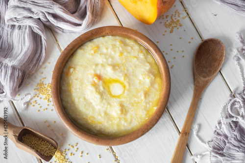 Konstfotografi Delicious breakfast: millet porridge with pumpkin and a piece of butter in a wooden plate on a white background
