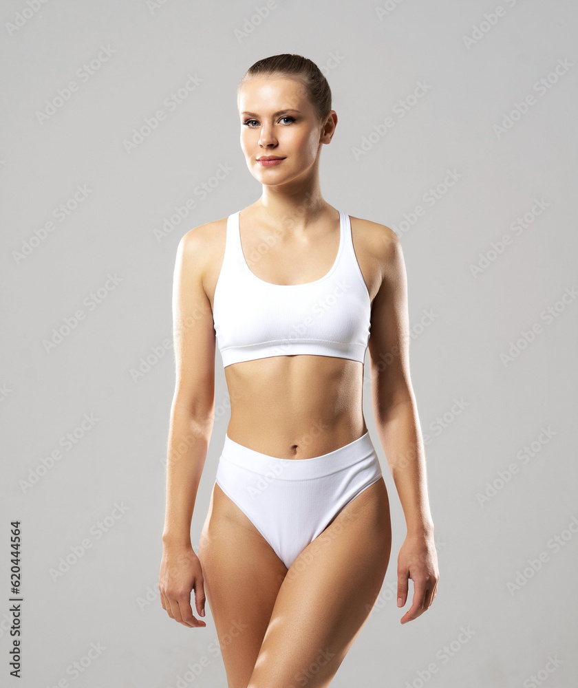 Fototapeta premium Young and beautiful slender girl in white swimsuit posing over white background. Healthcare, diet, sport and fitness concept.