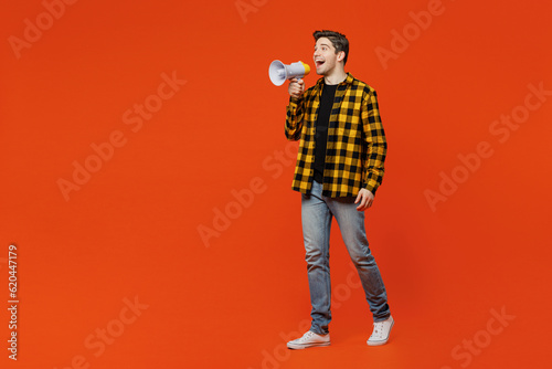 Full body young caucasian man he wear yellow checkered shirt black t-shirt hold in hand megaphone scream announces discounts sale Hurry up isolated on plain red orange background. Lifestyle concept. © ViDi Studio