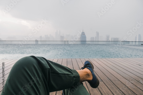 Canvas Print View of the metropolis of Kuala Lumpur, from the roof of a skyscraper with a swimming pool, in the foreground the traveler's legs