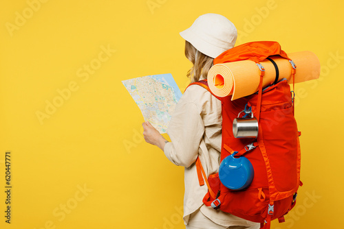 Side view young happy cheerful woman carry backpack with stuff mat hold map isolated on plain yellow background. Tourist leads active lifestyle walk on spare time Hiking trek rest travel trip concept #620447771