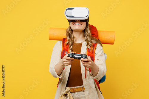 Young woman carry backpack with stuff mat watching in vr headset pc gadget with joystick console isolated on plain yellow background. Tourist walk on spare time. Hiking trek rest travel trip concept. #620447777