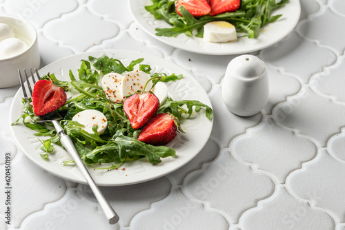 Salad with mozzarella with strawberries, mozzarella and arugula. Healthy light summer salad modern styling on white tile background text space