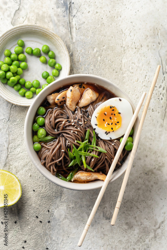 Asian soba noodle soup, with chicken, boiled egg, sesame seeds, green pea and green onion served with chopsticks. Top view, flat lay, text space