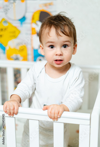 Small baby boy standing in bed. Portrait of child playing in crib.